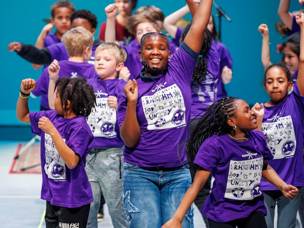 BalletX Dance eXchange students performing on stage with bright smiling faces
